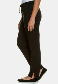 Zwarte stretchbroeken met een tailleband met koord, met gespleten zoom, gemaakt van een zachte stof, geschikt voor casual of loungewear.