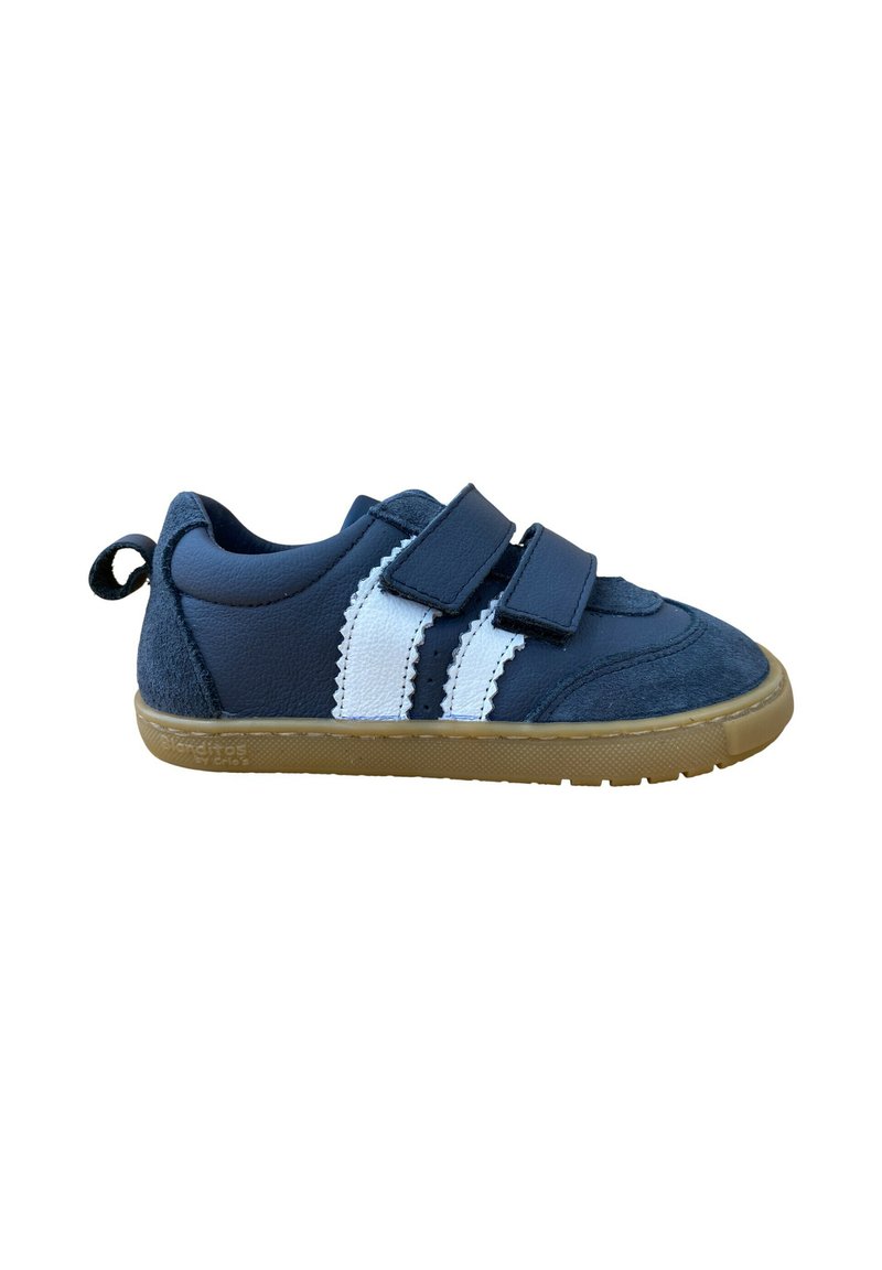 Zapatilla deportiva azul con rayas blancas, correas de velcro y parte superior texturizada. Suela de goma con un pequeño tirador en el talón para facilitar su uso.