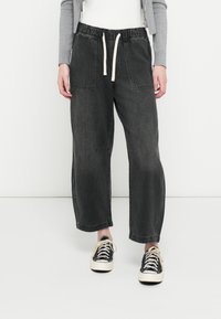 Σκούρο γκρι τζιν παντελόνι jogger με ελαστική μέση και κορδόνι, με δύο μπροστινές τσέπες και φαρδιά γραμμή. Φοριέται με ασπρόμαυρα αθλητικά παπούτσια.