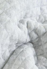 Hellgrauer, gestepptes Textil mit einer sanften, strukturierten Oberfläche. Verfügt über ein Rauten-Muster und eine glatte Oberfläche, die zum Berühren einlädt.