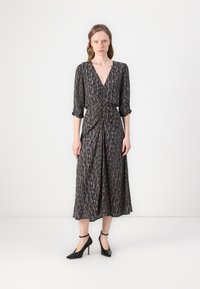 Dunkel gemustertes Midi-Kleid mit tiefem V-Ausschnitt, geraffter Taille, Dreiviertelärmel und fließendem Rock. Kombiniert mit schwarzen High-Heels.