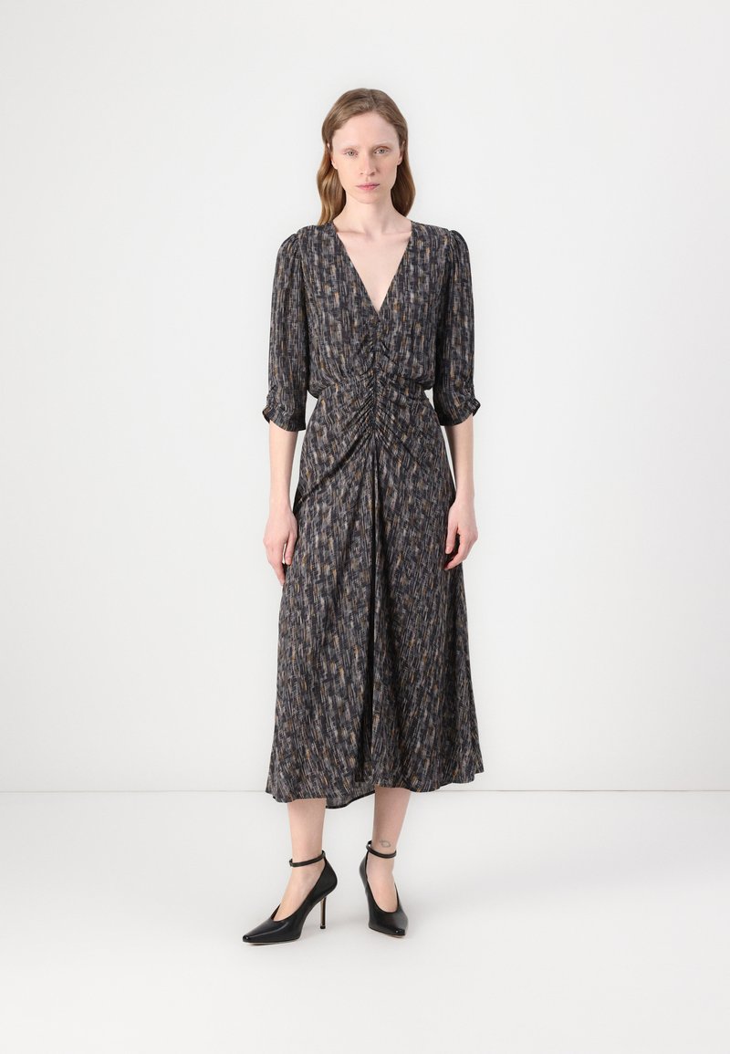 Dunkel gemustertes Midi-Kleid mit tiefem V-Ausschnitt, geraffter Taille, Dreiviertelärmel und fließendem Rock. Kombiniert mit schwarzen High-Heels.