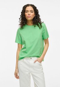 Grøn bomulds T-shirt med rund halsudskæring og korte ærmer, parret med hvide teksturerede bukser med et subtilt mønster.