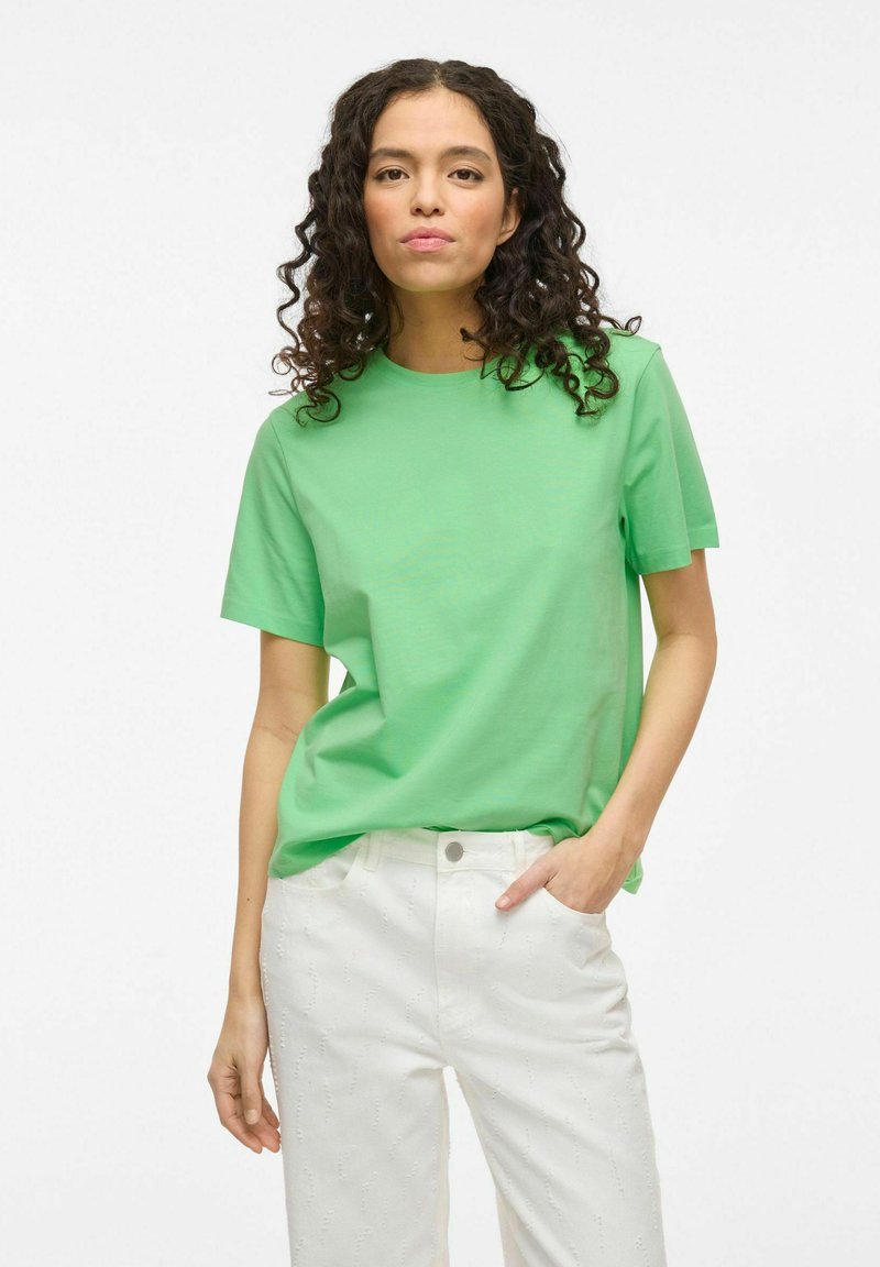 Grøn bomulds T-shirt med rund halsudskæring og korte ærmer, parret med hvide teksturerede bukser med et subtilt mønster.