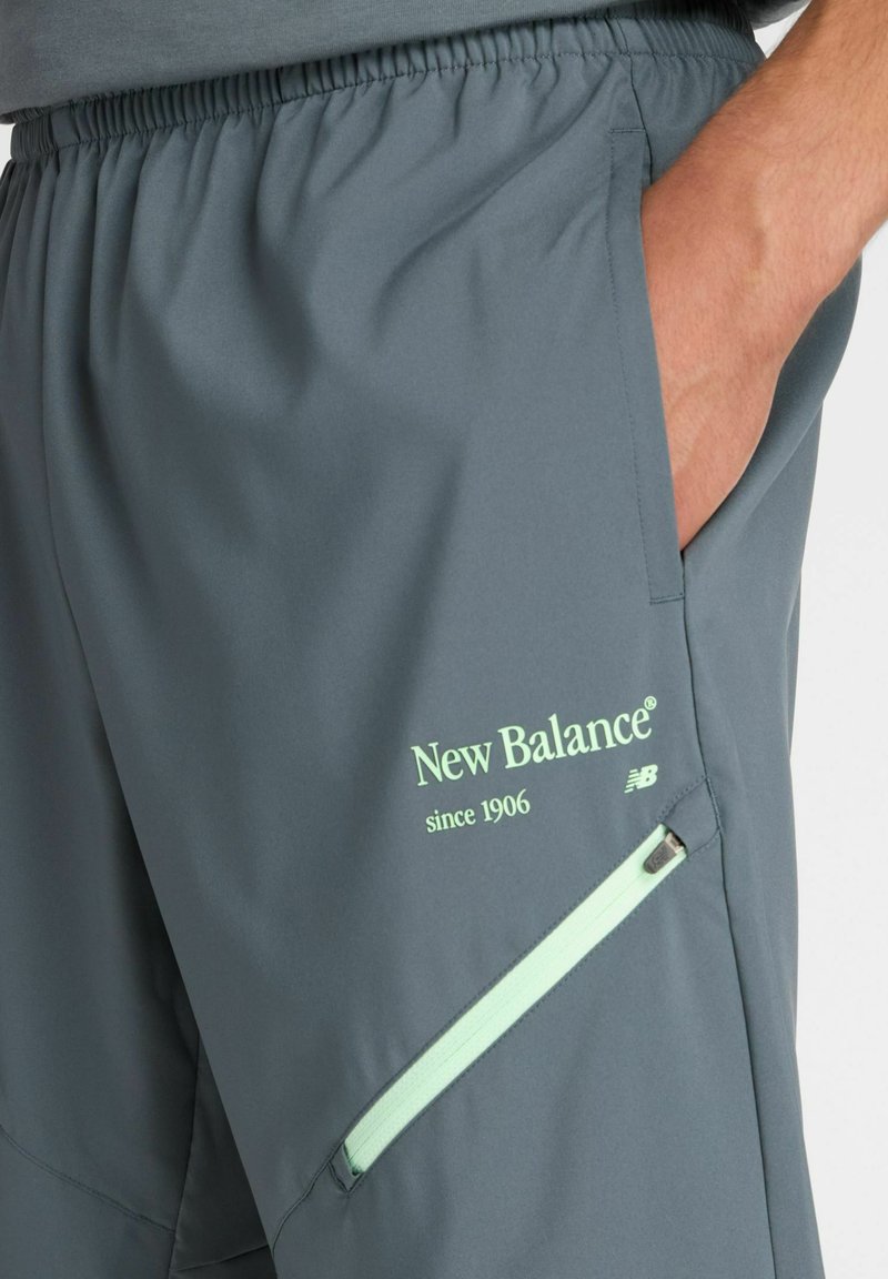 Gray athletic shorts made of lightweight fabric, featuring a mint green logo, side pockets, and a zippered pocket detail.