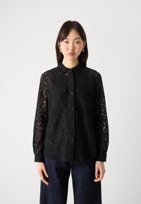 Black lace button-up shirt with a collar, long sleeves, two chest pockets, and intricate floral patterns throughout. Textured, semi-sheer fabric.