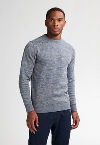 Suéter de punto gris-azulado con cuello redondo, patrón texturizado y puños acanalados. Llevado con jeans azul oscuro. Diseño simple y casual.