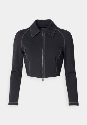 Kuttet svart jakke i elastisk stoff, med krage og glidelås foran, samt kontrasterende hvite sømmer langs sømmene.