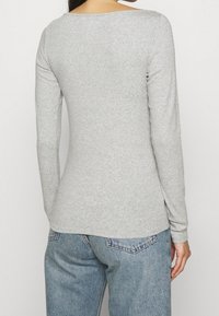 Šedá dlouhá košile z měkké tkaniny s širokým výstřihem a přiléhavým střihem, v kombinaci se světle modrými džínami.