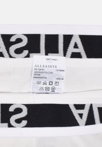 Vit tyg med ett svart elastiskt midjeband som visar "ALLSAINTS" i vit text. Skötselråd synligt på insidan.