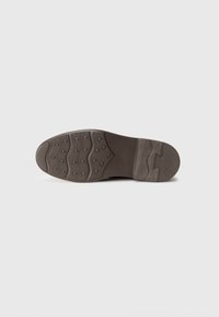 Suola di scarpa in gomma marrone con texture a motivo, caratterizzata da punti e scanalature sollevati per la trazione. Design sagomato nella zona del tallone.