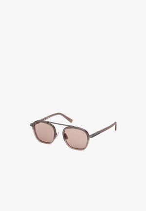Gafas de sol grandes en color marrón con montura transparente marrón y lentes marrones claros. Cuentan con patillas delgadas con detalles metálicos.