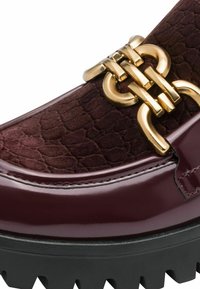 Burgunderfarbene Slipper mit glänzender Lackoberfläche, strukturiertem Obermaterial, goldfarbenen Hardware-Details und einer massiven, schwarzen Profilsohle.