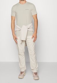 Světlá béžová košile s krátkým rukávem a logem Columbia, v kombinaci se světlými béžovými kalhotami. Měkký světlý svetr uvázaný v pase. Neformální obuv.