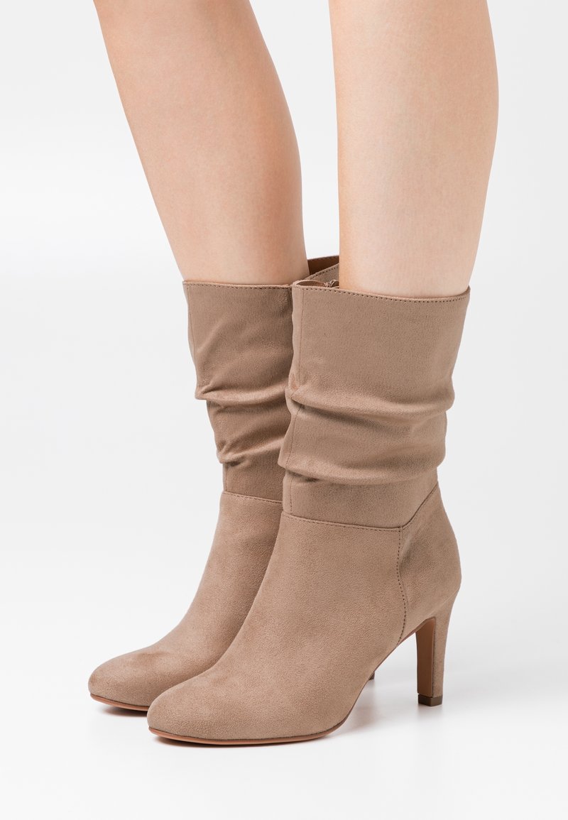 Botas de tobillo beige de ante suave, con punta redondeada y tacón afilado de 7 cm. La parte superior tiene una textura gathered cerca de la abertura.