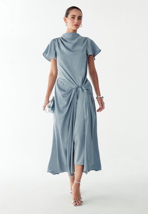 Jasnoniebieska sukienka midi z węzłem w talii, krótkimi falującymi rękawami i gładką, satynową fakturą. Srebrne akcenty dopełniają wygląd.