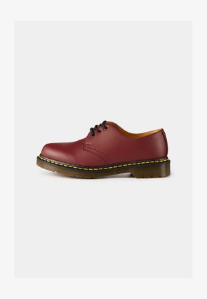 Chaussure en cuir rouge avec lacets, à bout rond, surpiqûre jaune le long de la semelle et accent jaune autour de la base. Semelle extérieure en caoutchouc durable.