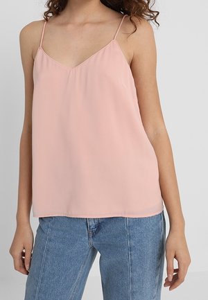 Woman wearing a light pink sleeveless V-neck cami top with thin straps paired with light blue high-waisted jeans, against a plain background.
