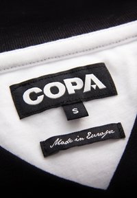 Black and white clothing labels showing brand name COPA, size S, and "Made in Europe" text on a black and white fabric garment.