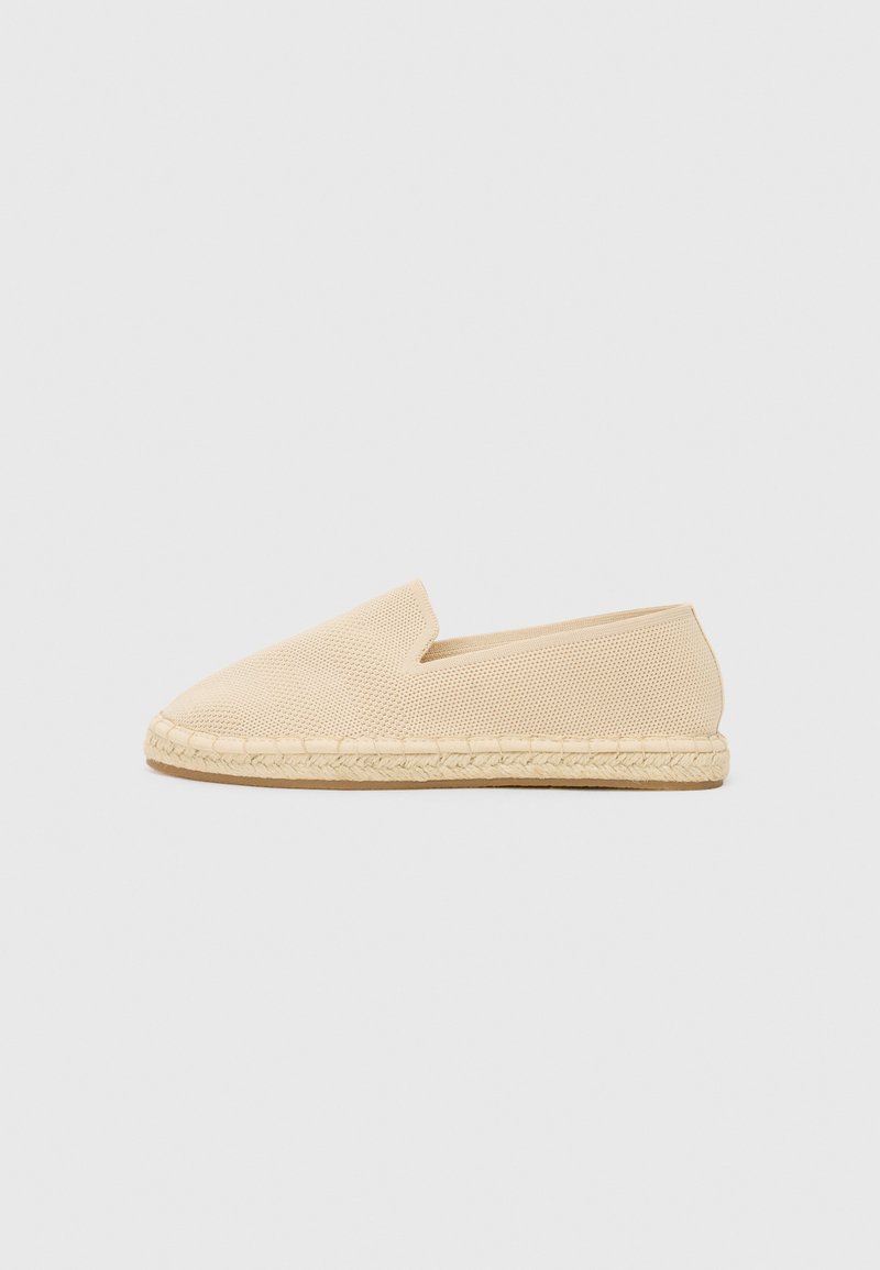 Beige instap espadrille met een bovenwerk van gestructureerde stof en een jute gevlochten zool. Rond neusontwerp met minimale detaillering.