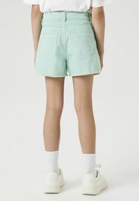 Mintgroene denim shorts met een franjeszoom, met twee achterzakken en een hooggewaist ontwerp. Gemaakt met witte sneakers en sokken.