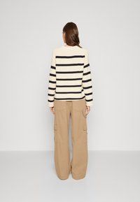 Maglione lavorato a maglia con strisce crema e navy, caratterizzato da maniche lunghe. Abbinato a pantaloni cargo beige larghi con tasche laterali.