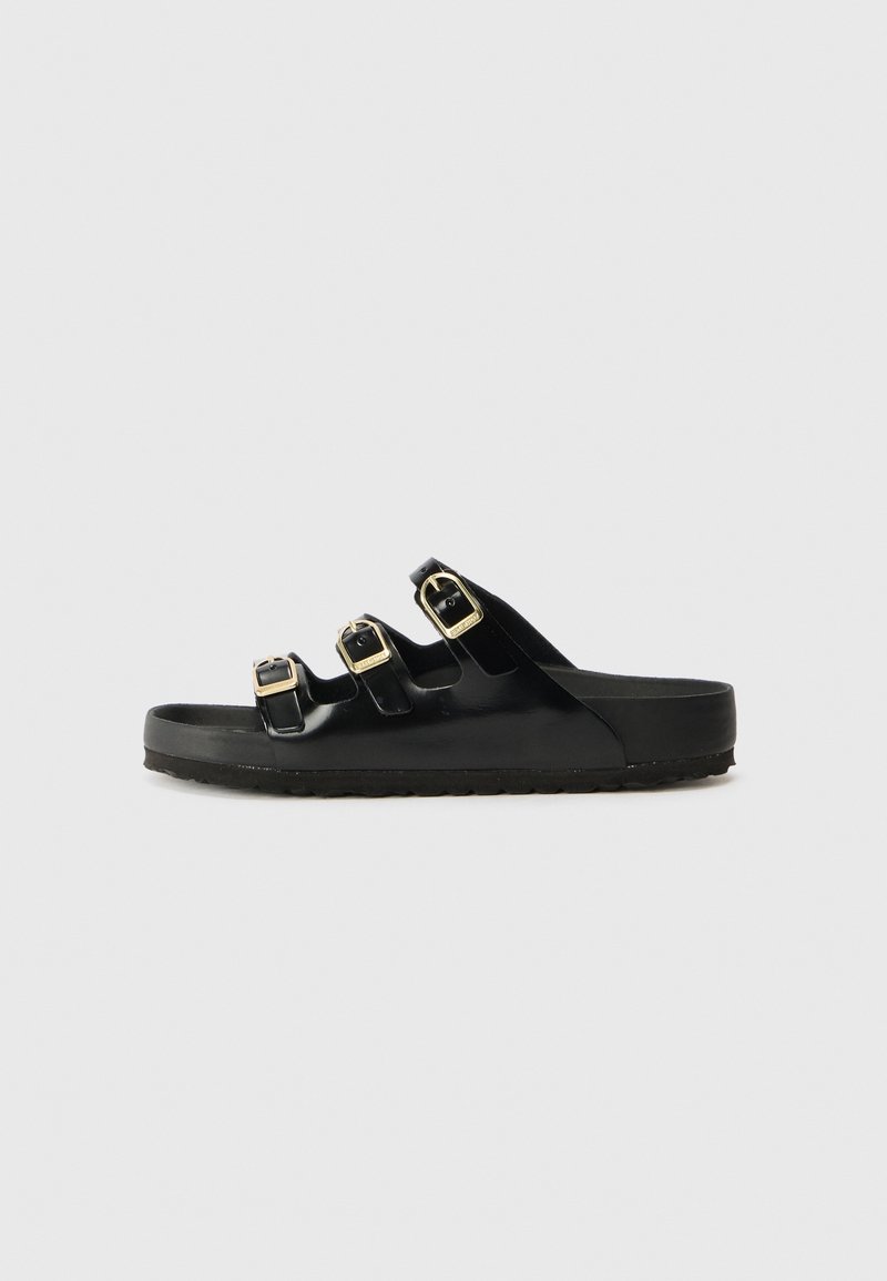 Sandale slide noire avec trois brides ajustables à boucles dorées et semelle plate sur fond gris clair.