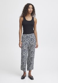 Un débardeur noir associé à un pantalon large crème avec un motif abstrait bleu marine. Les chaussures sont des ballerines noires avec un détail en nœud.