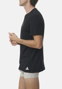 Black cotton T-shirt with short sleeves, crew neckline, and a white logo accent at the hem. Worn over light grey boxer shorts.