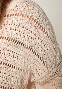 Jasnoróżowy sweter z dzianiny z otwartym wzorem, teksturowymi ściegami oraz szerokim, zaokrąglonym dekoltem.