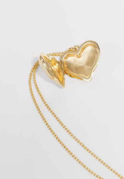 Ciondolo a forma di cuore in oro su una catena d'oro. Il ciondolo è liscio e lucido, presenta un perno e un design aperto con un interno riflettente.