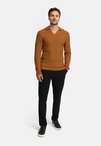 Brauner gestrickter Pullover mit vertikalen Rippen und V-Ausschnitt, kombiniert mit schwarzen Hosen und dunklen Sneakers. Der Stoff wirkt strukturiert.