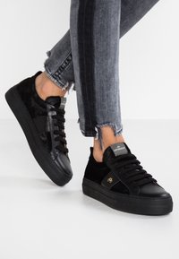 Svarta sneakers som har en blandning av läder och konstpäls, låg design, texturerade detaljer och en synlig logotyp på tungan.