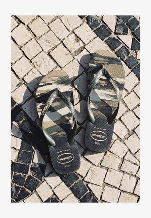 Paar Camouflage-Havaianas Flip-Flops, die auf einem schwarz-weißen Mosaiksteinpflaster liegen.