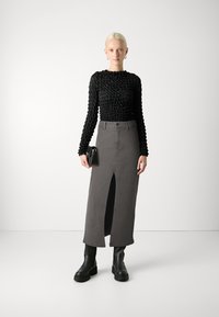 Svart teksturert langermet topp med en tettsittende design, sammen med en grå høy midje skjørt med en frontsplitt. Svart plattformstøvler og veske.