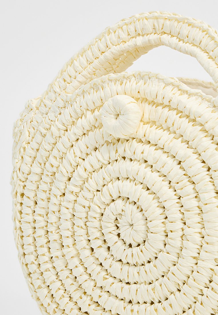 Bolso de paja circular en un amarillo claro, con tejido en espiral, una superficie texturizada y un detalle de botón redondo en el lateral. Los asas están integradas.