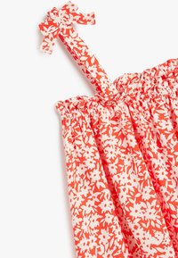 Bomulds kjole med orange og hvidt blomsterprint, der har en smocket bodice og en sløjfedetail på en enkelt strop.