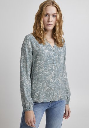 Chemisier bleu clair à manches longues avec un motif floral blanc. Il présente des manches longues avec des poignets froncés et un décolleté en V. Tissu doux au toucher.