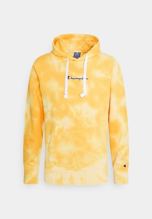 Keltainen ja valkoinen tie-dye Champion-huppari valkoisilla nyöreillä, etutaskulla ja Champion-logo rinnassa sekä vasemman hihan resorissa.