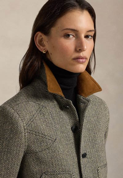 Płaszcz w jodełkę z brązowym kołnierzem zamszowym, czarnymi guzikami i dopasowanym czarnym golfem, na neutralnym tle.