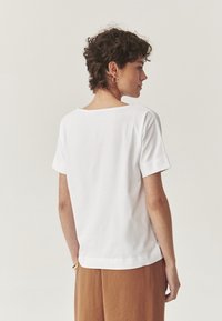 T-shirt blanc en coton à manches courtes, avec un col large, une coupe décontractée et un ourlet arrondi, associé à un pantalon en lin marron.