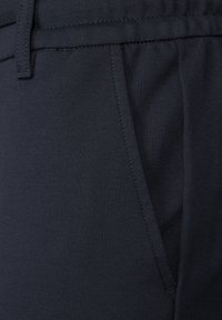 Pantalons taillés bleu marine foncé avec une texture lisse, dotés d'une poche latérale, de passants de ceinture et de coutures soignées le long de la taille.