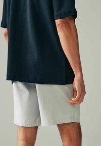 Navyfarbendes Baumwoll-T-Shirt kombiniert mit hellgrauen Shorts. Das T-Shirt hat eine lockere Passform, die Shorts sind knielang, mit glatter Textur und ohne Muster.