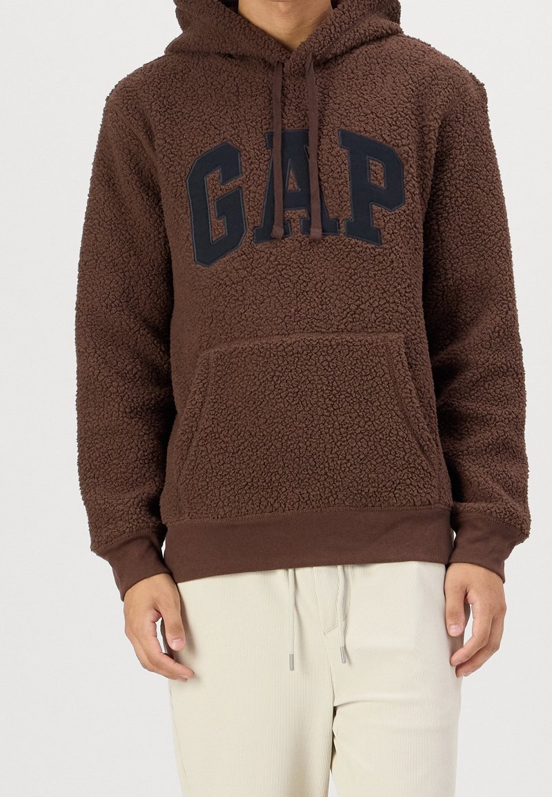 Hnědá mikina z fleecu s kapsou klokanem, s tmavě modrým logem "GAP" na hrudi a kapucí se šňůrkou. Měkká, strukturovaná látka.