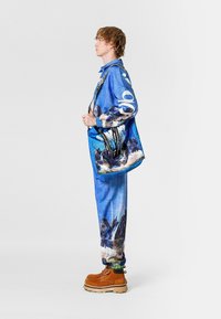 Chaqueta y pantalones azul con estampado de montañas; botas marrones; correa blanca y negra; textura suave; ajuste casual.