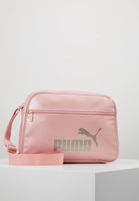 Borsa in finta pelle rosa con finitura lucida, dotata di una tasca anteriore con zip e un grande logo Puma argento. Include una tracolla coordinata rosa.
