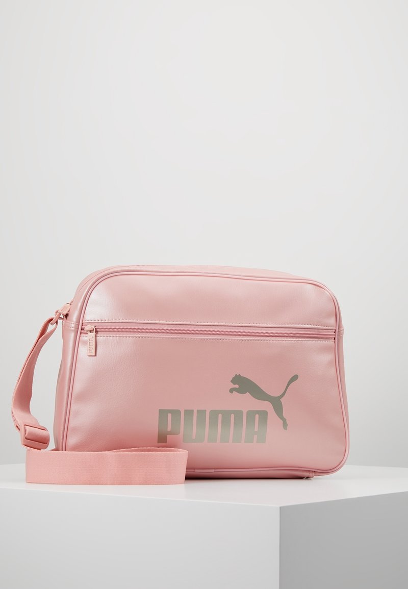 Borsa in finta pelle rosa con finitura lucida, dotata di una tasca anteriore con zip e un grande logo Puma argento. Include una tracolla coordinata rosa.