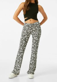 Pantalones florales en blanco y negro con cintura alta, diseño de pierna recta y patrón de margaritas; combinados con un top corto negro acanalado.