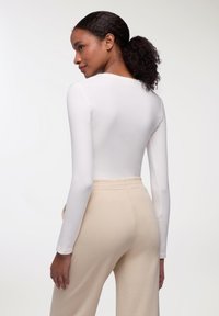 Bodysuit bianco a maniche lunghe con collo rotondo, abbinato a pantaloni tuta beige con vita elastica. Tessuto liscio con cuciture minime e senza fantasie.