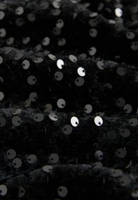 Schwarzer Stoff mit flachen, runden Pailletten in glänzender Optik, dicht angeordnet über einer strukturierten Oberfläche, die ein weiches und schimmerndes Erscheinungsbild erzeugt.